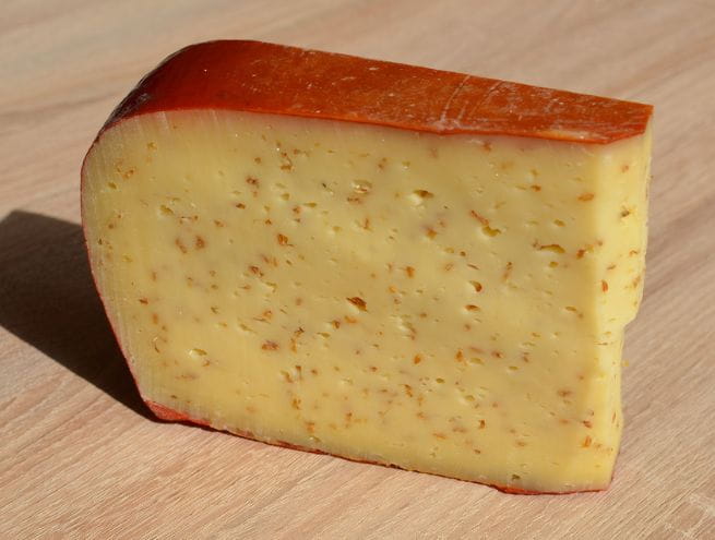 Semi-hard cheese infused with mustard seeds, displaying a golden hue and speckled texture