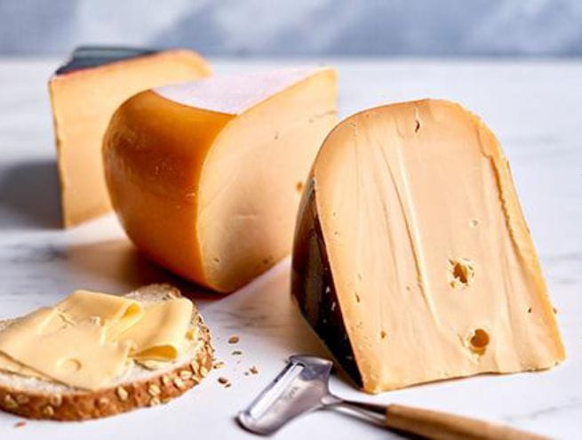 Selection of aged cheeses on a marble surface, with a slice of bread and butter in the foreground.