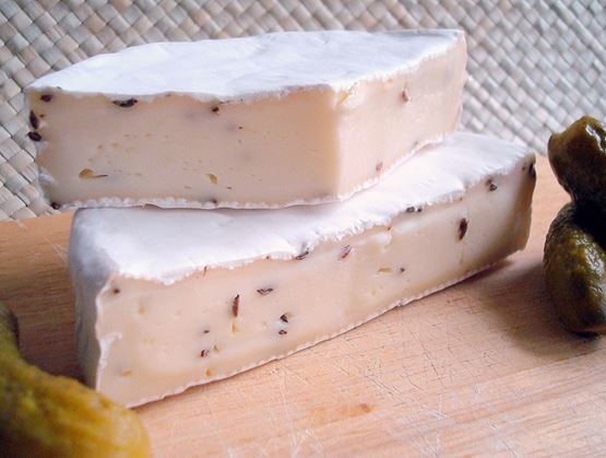 Fromage à pâte molle en morceaux avec croûte blanche, accompagné de cornichons.