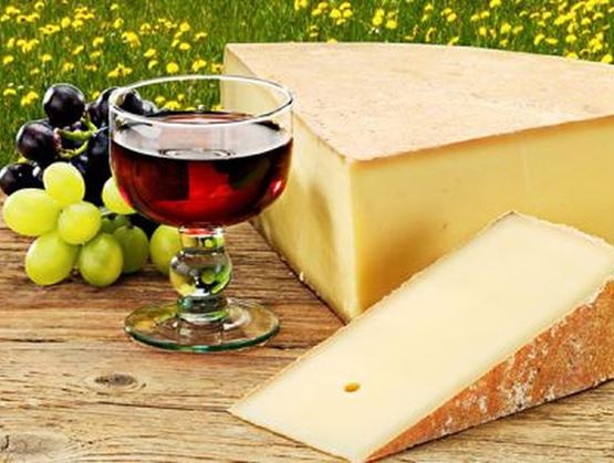 Fromage avec un verre de vin rouge et des raisins sur une table en bois.