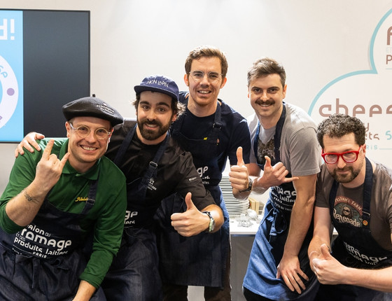 Un groupe de chefs posant ensemble avec des sourires, vêtus d'uniformes de cuisine lors d'un événement gastronomique.